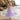 Young girl in a purple lace dress standing on a beach with ocean waves and rocks in the background.