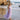 Young girl in a purple lace dress standing on a beach with waves and rocks in the background